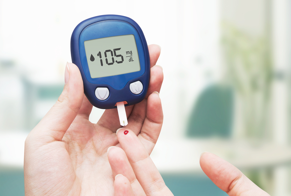 photo of hand holding a glucometer near a finger with drop of blood on it